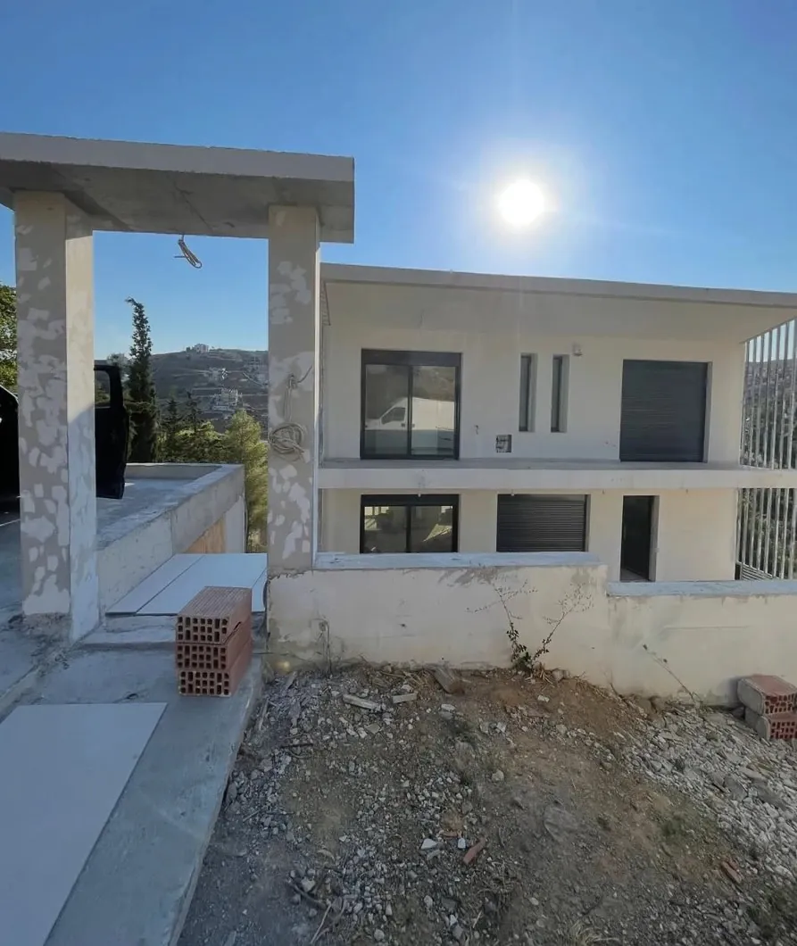 Νέα διώροφη κατοικία υπό κατασκευή, με τα κουφώματα τοποθετημένα και τον περιβάλλοντα χώρο ακόμη σε χώμα.